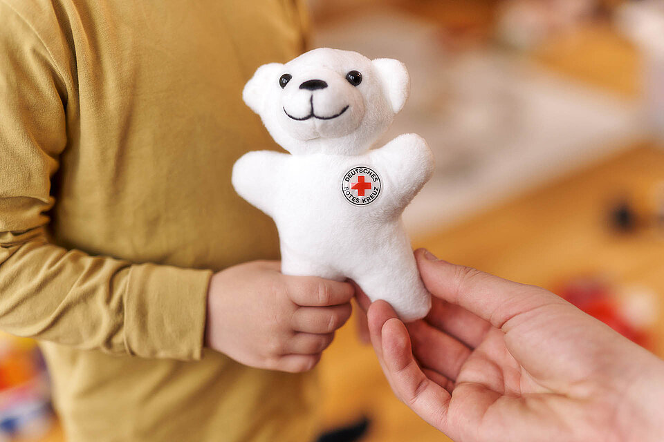 Kinderhand greift Teddy aus Erwachsenenhand