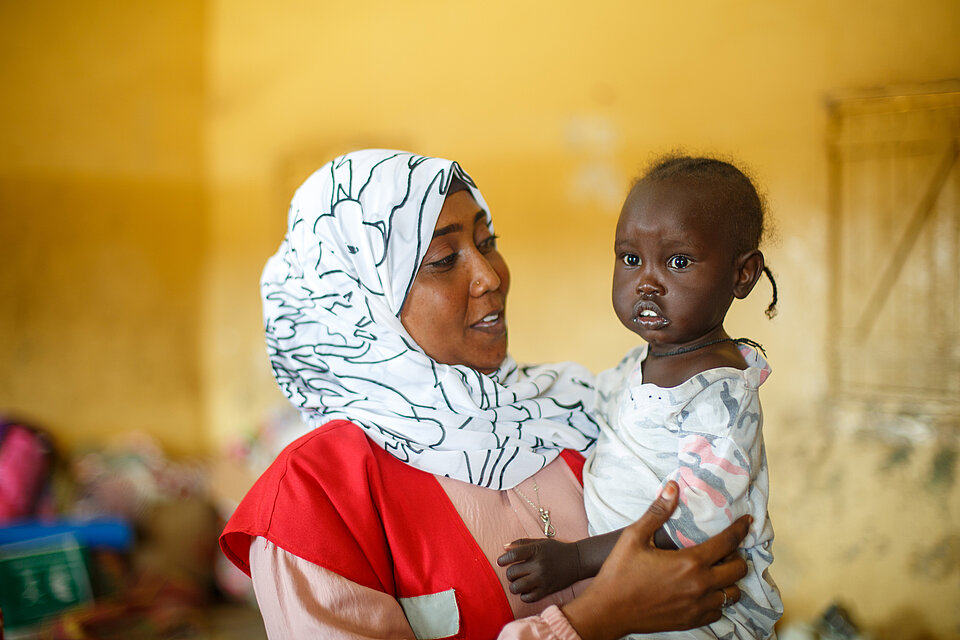 Bewaffneter Konflikt im Sudan: Freiwillige vom Sudanesischen Roten Halbmond mit einem Kleinkind von Binnenflüchtlingen auf dem Arm