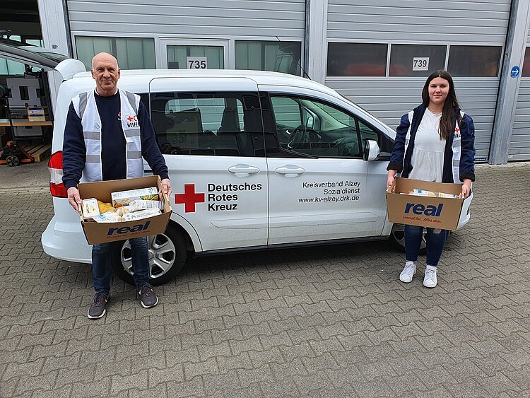 Einkaufsservice des DRK Ein DRK-Mitarbeiter und eine DRK-Mitarbeiterin stehen vor einem Lieferwagen und haben Kartons mit Lebensmitteln in der Hand