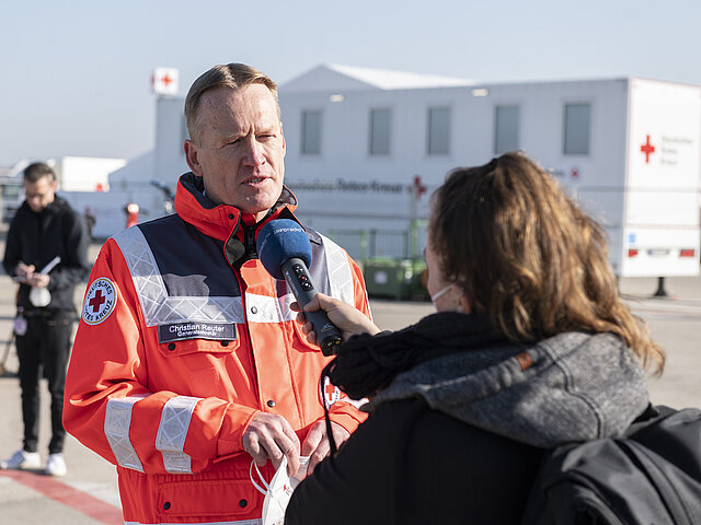 DRK-Generalsekretär Christian Reuter steht in DRK-Einsatzkleidung im Freien und wird von einer Frau interviewt