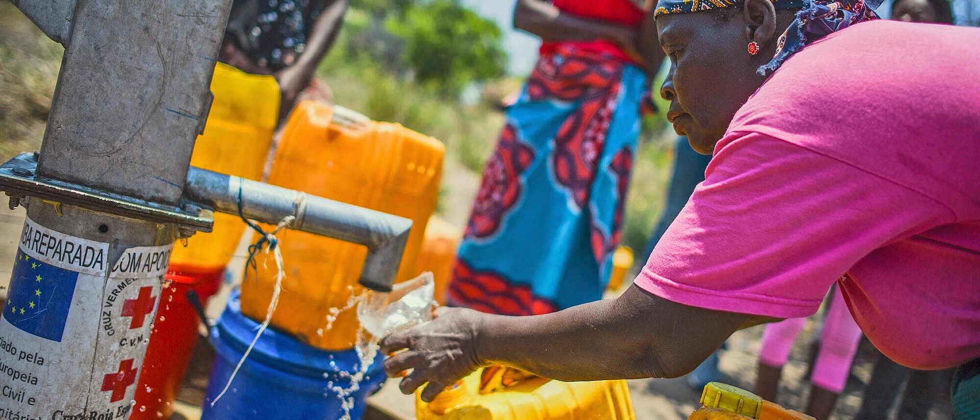 Wasserstelle in Mosambik Frau gießt an Wasserstelle Wasser in Glas