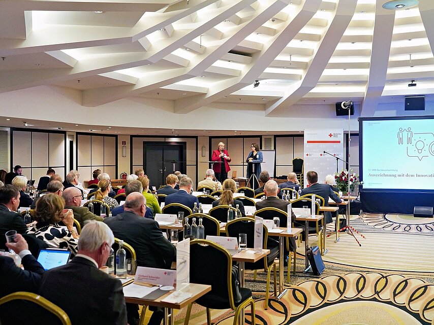 Verleihung des DRK-Innovationspreises 2023 im Rahmen der Bundesversammlung: DRK - Vizepräsidentin Ulrike Würth und Gisela Wedler (Teamleiterin im Bereich Jugend und Wohlfahrt beim DRK-Generalsekretariat) vor den Teilnehmern.