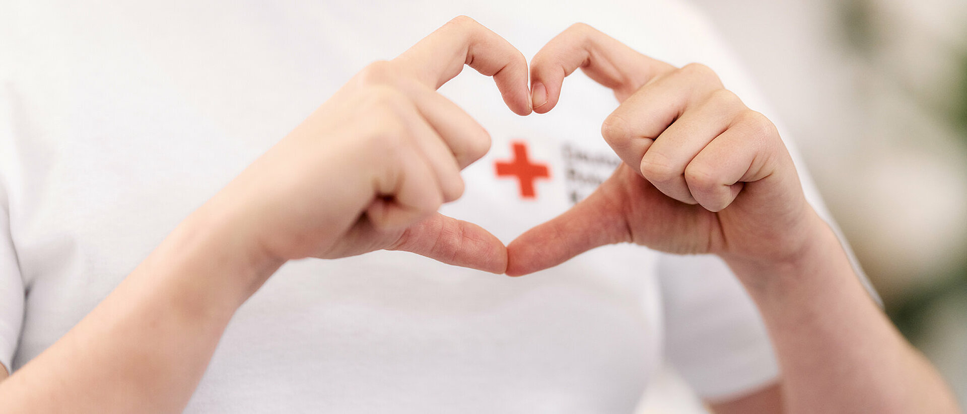 Corporate Volunteering: Spenden von Vergütungen aus Liebe zum Menschen Corporate Volunteering in Form von Spenden: Hände formen ein Herz um ein DRK-Logo