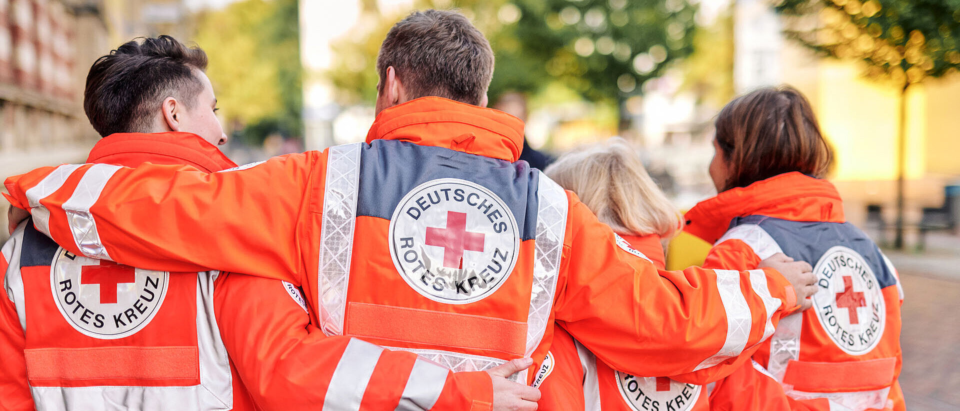 Teamarbeit im Einsatz Vier DRKler in Einsatzjacken legen Arme über Schultern