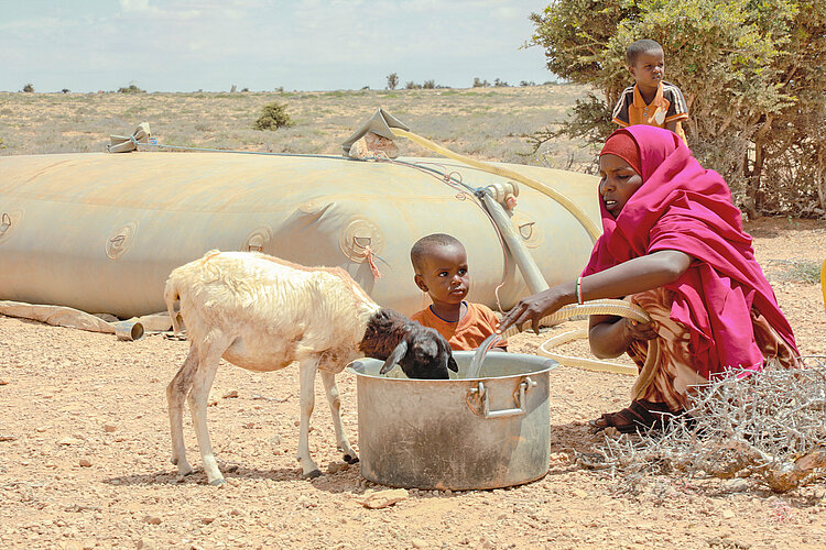 Frau mit Kind und Nutztier an einer Wasserstelle in Somalia 