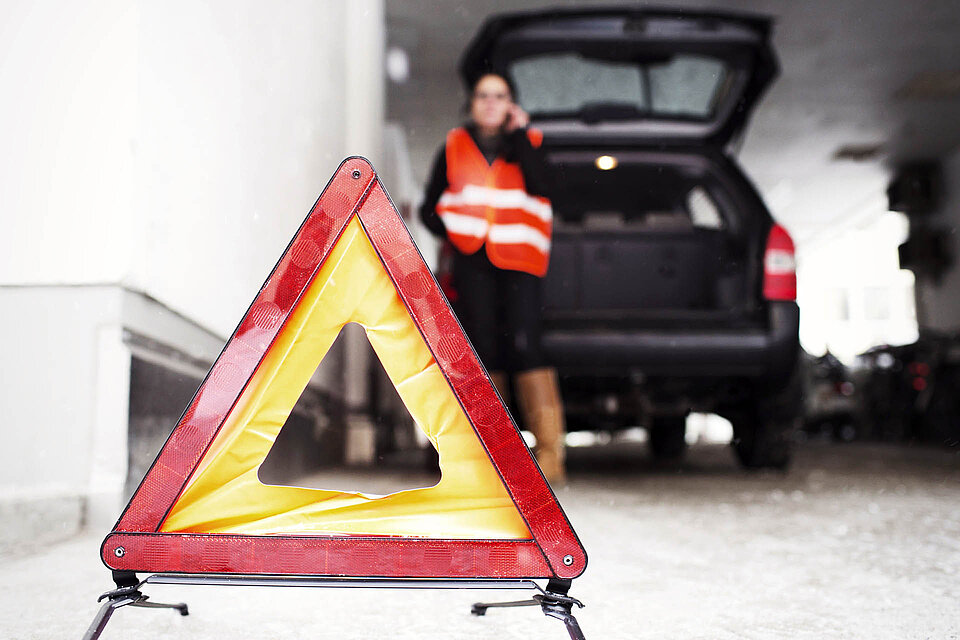 Notruf und Warndreieck Warndreieck vor Auto und telefonierender Frau