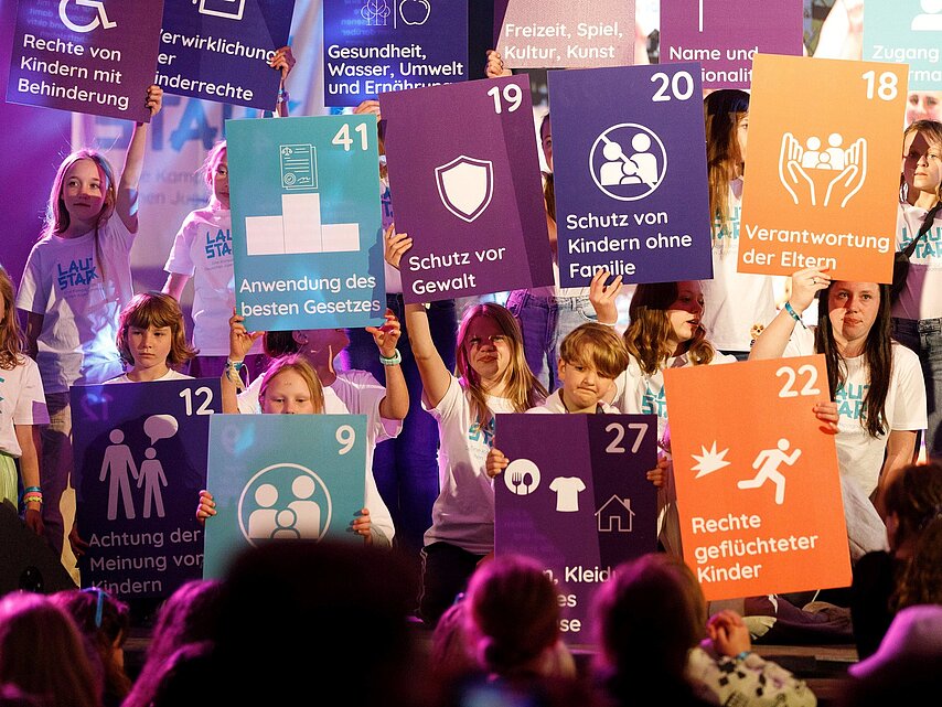 Viele Kinder des Jugendrotkreuzes halten bunte Plakate mit den Kinderrechten hoch.