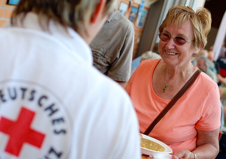 Betreuungsdienst_DRK_Katastrophe.jpg Man sieht den Rücken einer Helferin vom DRK mit dem DRK-Logo auf dem T-Shirt und eine ältere Dame die lächeltinsaetze, Flut, Überschwemmung, Naturkatastrophe, Katastrophe, Überflutung, Evakuierung, Versorgung, Flutkatastrophe