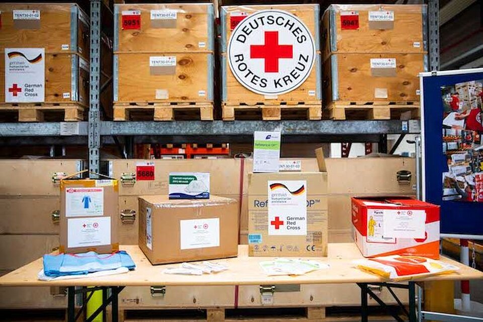 DRK-Hilfsgüter für den Libanon Verschiedene Pakete mit Hilfsgütern stehen vor einem Lagerregal mit weiteren Packkisten und verschiedenen Logos des DRK.