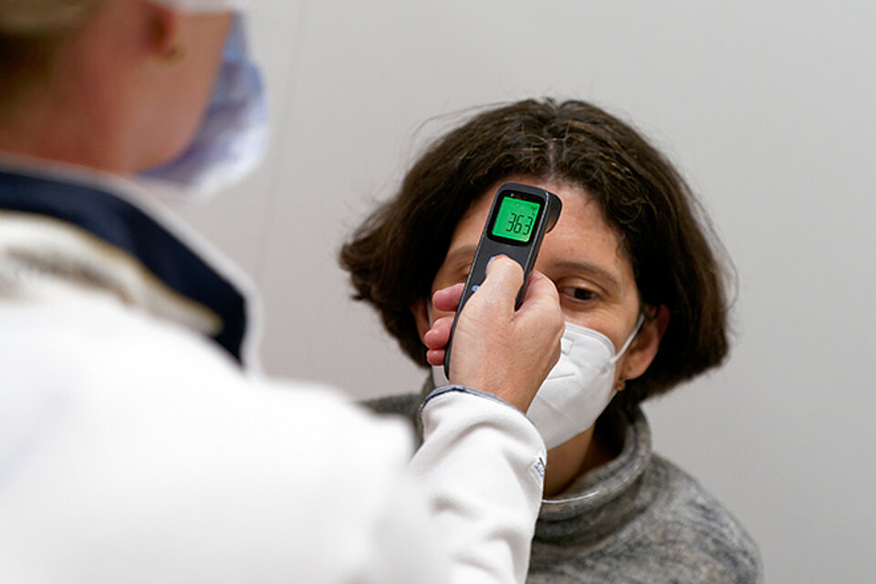 Temperatur messen Medizinische Fachkraft misst Temperatur an Stirn einer Frau