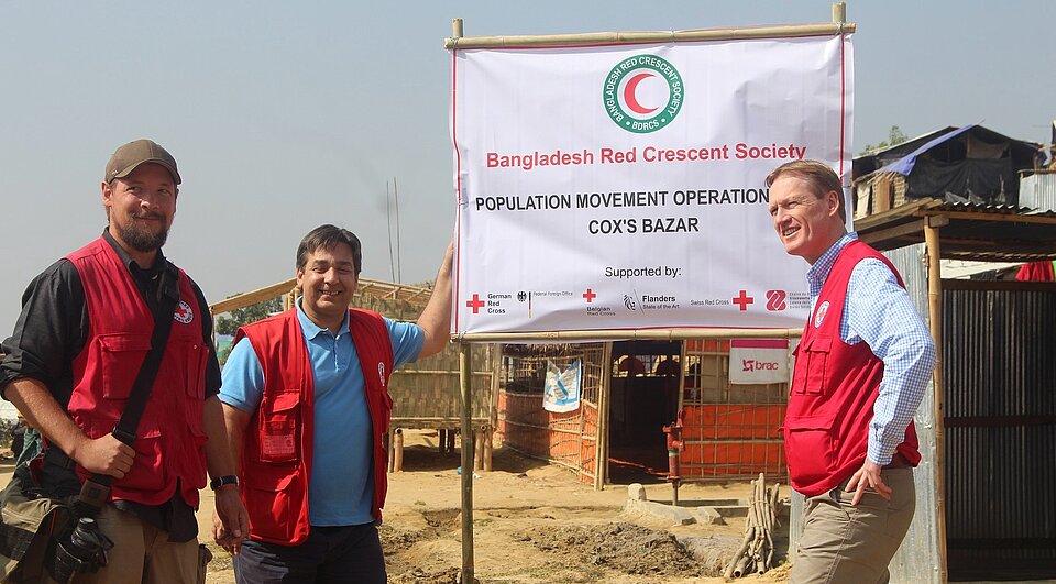 DRK-Generalsekretär Christian Reuter in Bangladesch DRK-Mitarbeiter stehen im Flüchtlingslager an einem Banner des Bangladesh Red Crescent