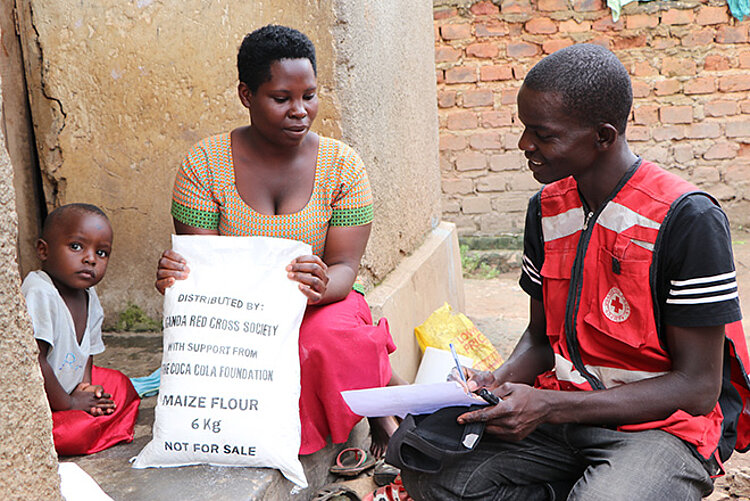 Nahrungsmittelspenden gegen Hunger bei Flüchtlingen in Uganda Rotkreuzler überreicht Frau in Uganda Nahrung