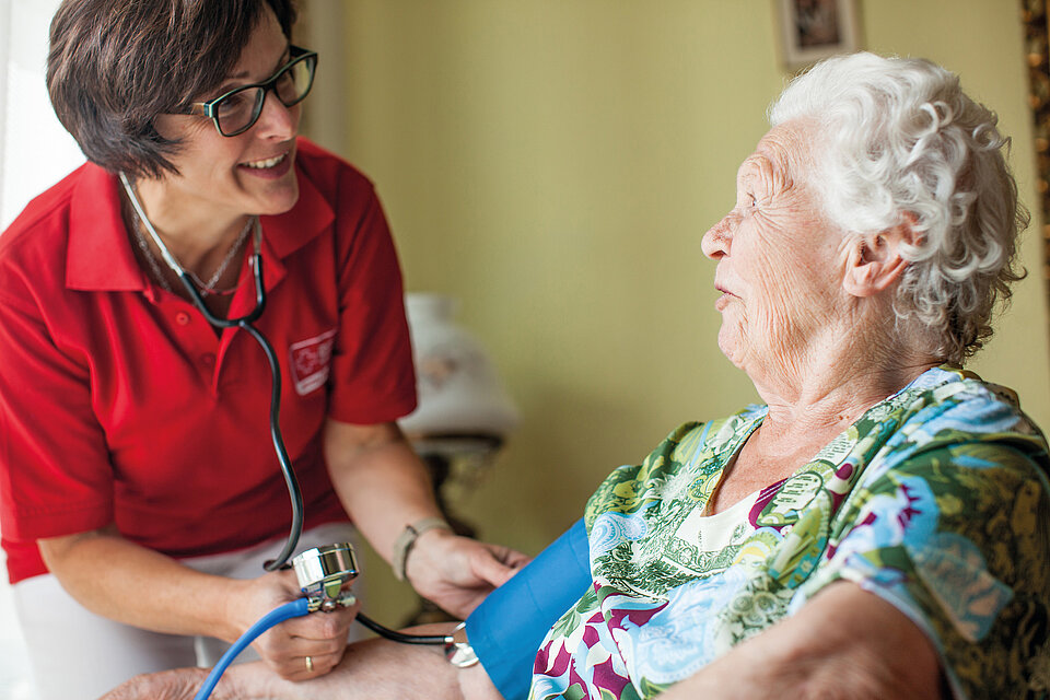 DRK-Mitarbeiterin bei einer Seniorin zuhause bei der Blutdruckmessung
