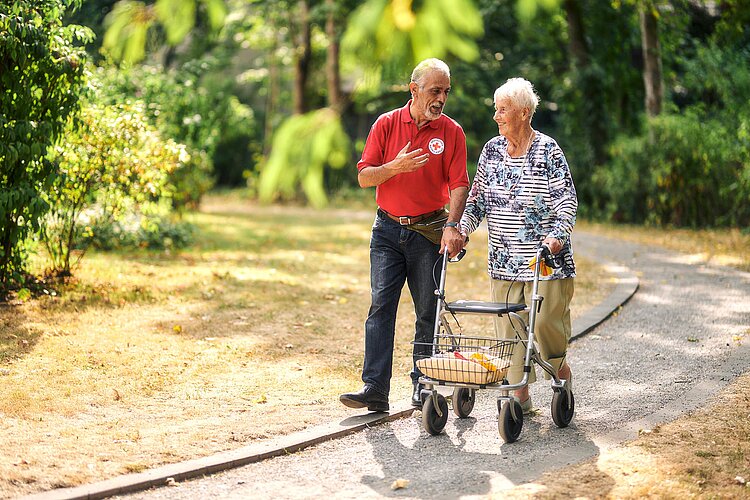 Rollator im Einsatz Pfleger und Seniorin mit Rollator spazieren durch Park