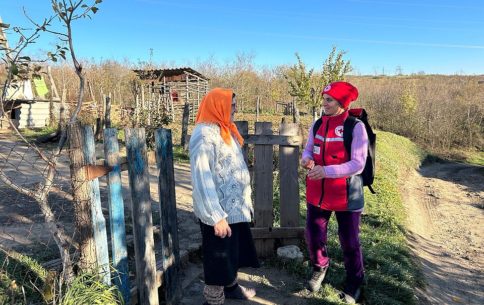 Mitarbeiterin des Ukrainischen Roten Kreuzes bei einem Hausbesuch bei einer älteren Frau. Gespräch am Gartentor