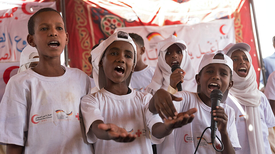 Projektbesuch im Sudan Kinder in weißen Projekt-Shirt singen