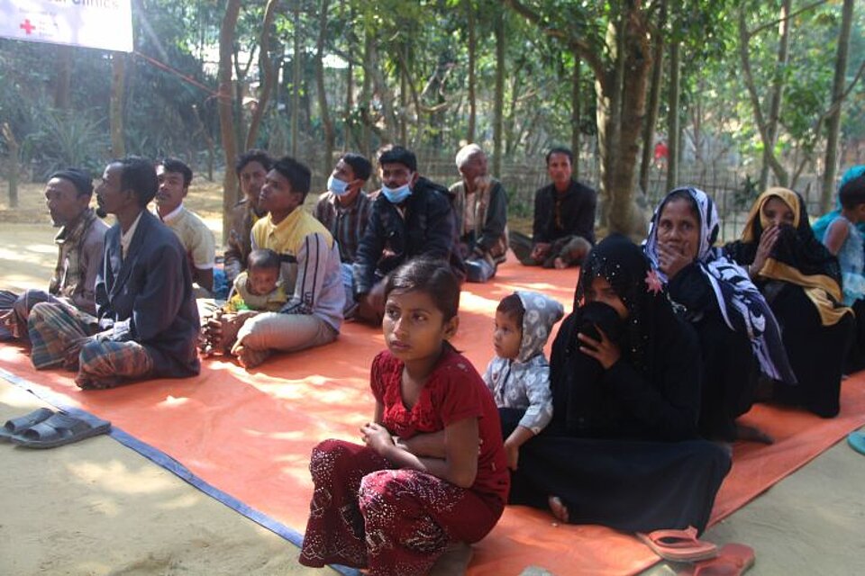 Flüchtlingshilfe in Bangladesch Menschen sitzen in Reihen auf Decke