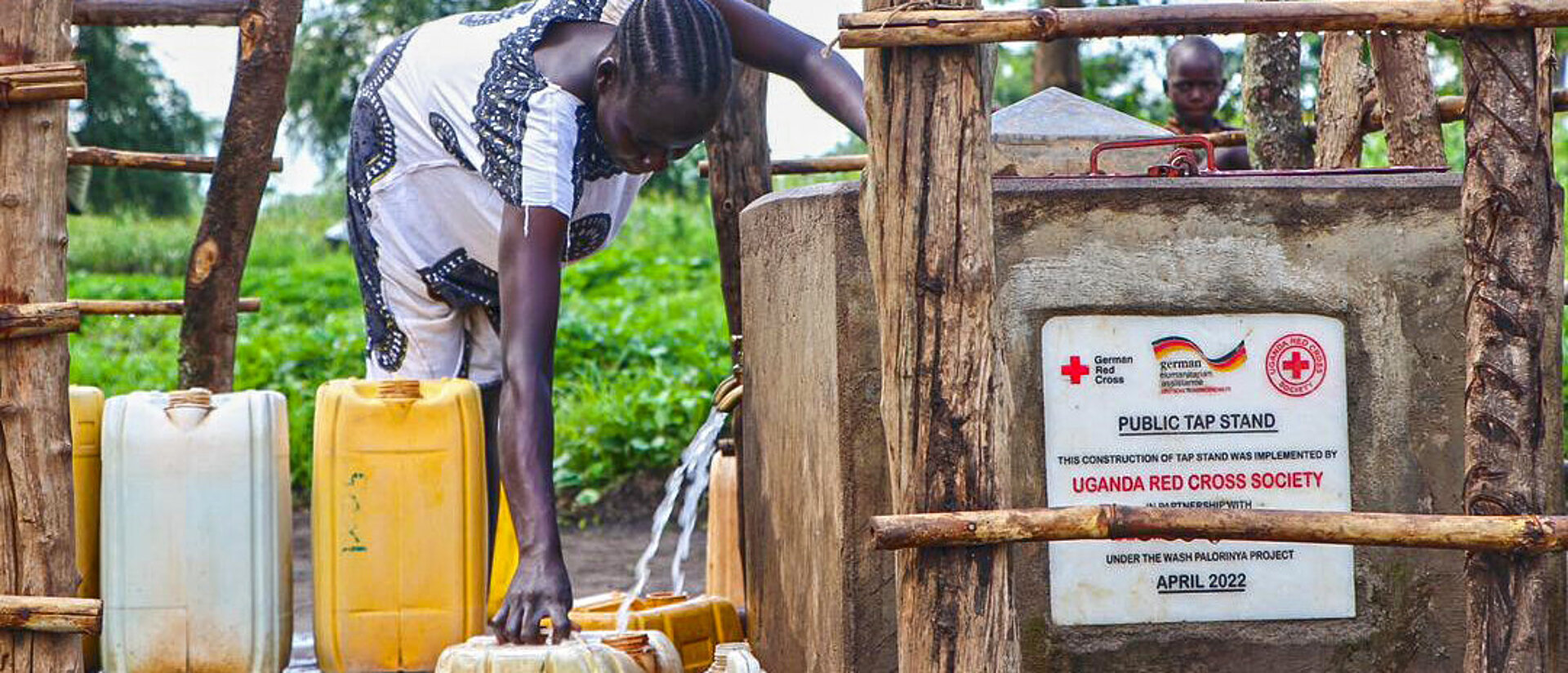 DRK-Hilfe in Uganda Frau gießt Wasser in Kanister an Wasserstelle