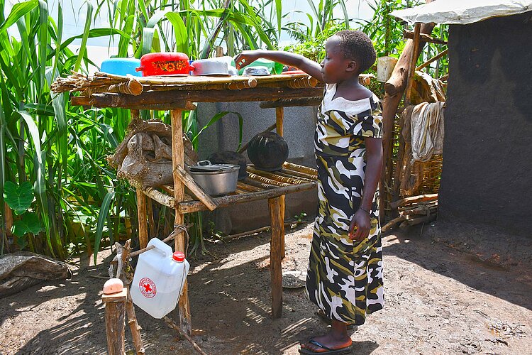 Rotkreuz-Hilfe in Uganda Mädchen steht an Außenküche aus Holz