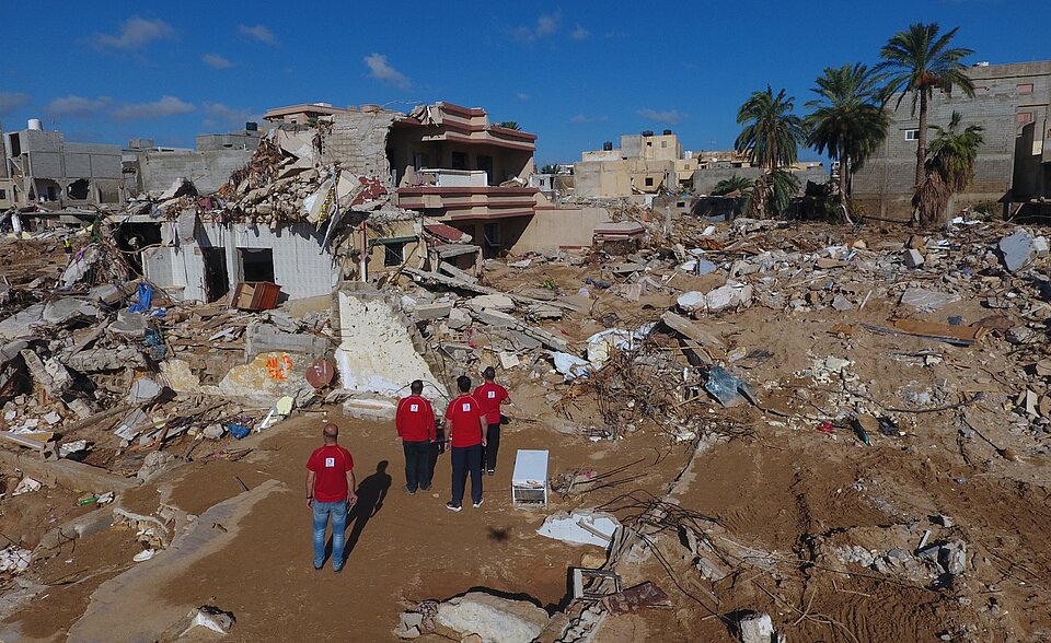 Zerstörtes Viertel in der libyschen Stadt Derna. Ausblick auf ein Gebiet mit völlig zerstörten und Helfern des Libyschen Roten Halbmonds im Vordergrund