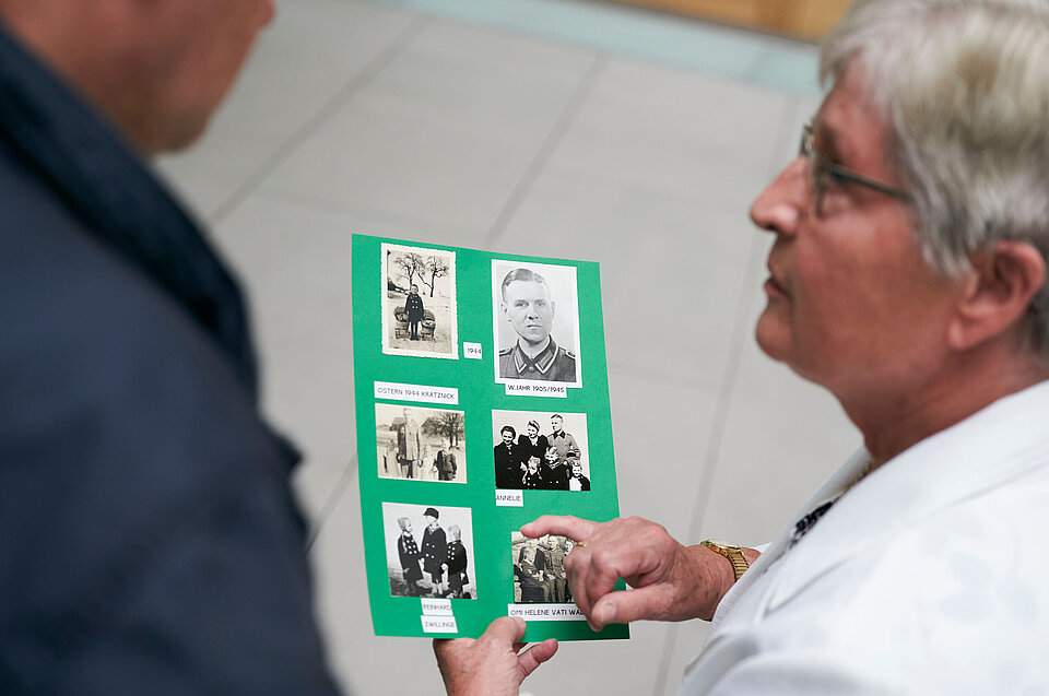 Person, die Anfrage nach im 2. Weltkrieg vermissten Familienangehörigen stellte, zeigt einer anderen Person alte Fotos.
