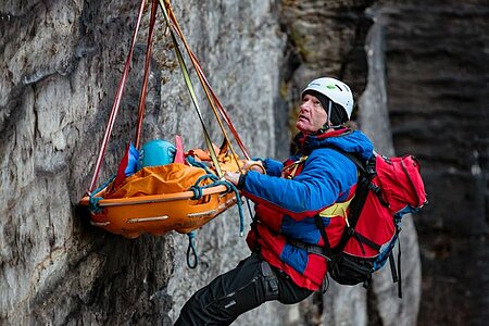 Ein Bergretter in Schutzkleidung ist an einem Felsen abgeseilt