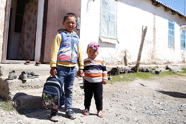 Kinder in Kirgistan kirgisische Kinder mit Rucksack vor Haus